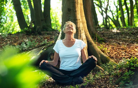 blonde older woman sitting cross-legged outdoors in the forest - ecotherapy